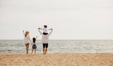 Deniz sahilinde günbatımının tadını çıkaran bir ailenin hoş bir sahnesi. Baba, oğlunu omuzlarında taşır ve tasasız bir birliktelik portresi yaratır. Aile sahilde tatilde.