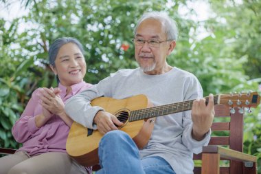 Asyalı yaşlı bir çift gitar çalarken karısı dışarıda birlikte şarkı söylüyor, Faaliyet ailesinin sağlık hizmetleri emeklilik hayatı boyunca eğleniyor yaşlılarla eğleniyor.
