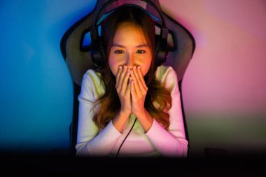 Asyalı mutlu oyuncu oyunu bilgisayar neon ışığı ile çevrimiçi video oyunları turnuvası düzenliyor, oyun kulaklığı takan gülümseyen genç kadın evde canlı yayın oyunları oynamak niyetinde, yazı tipi görünümlü