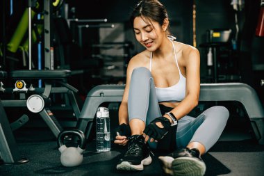 Sporcu genç Asyalı kadın spor ayakkabılarını giyerken spor aletlerinin ipini sıkıyor. Görüntü fitness ve sağlığa adanmışlığın mesajını gösteriyor.