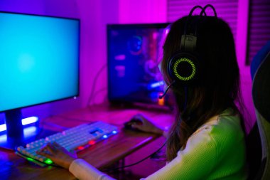 Masaüstü bilgisayarında çevrimiçi video oyunu oynayan Asyalı profesyonel oyuncu renkli neon ışıklı ışıklara, evde oyun oynamak için bilgisayar kullanan oyun kulaklıklı genç bir kadına sahiptir.