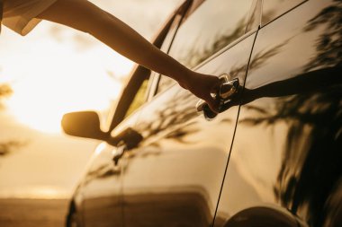 Gün batımında bir arabanın kapısını açan genç kadın elini kapat. Sürücü koltuğuna geçmek için el ele tutuşun. Seyahat konsepti