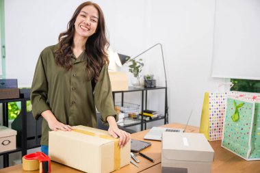 Asyalı genç bir kadın bantla bant paketliyor. İş kadını paketleri bant ile kapatıyor. Web sitelerinde ve sosyal medyada küçük bir iş kuruyor.
