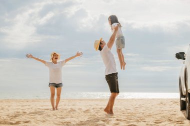 Üç mutlu aile kumsalda oynuyor, ebeveynler çocuklarını omuzlarında tutuyor çocukları havaya zıplıyor, tatiller yaz gezileri, aile günlerinin tadını çıkarıyorlar.