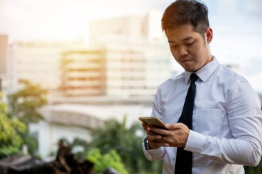 Genç Asyalı işadamı, yazılım geliştiricisi, telefon uygulaması kullanarak gülümsüyor. Ofis dışında yazılımı test etme başarısı. Memnun bir CEO 'nun portresi, ayakta duran, teknolojide ciddi.
