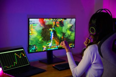 Asyalı oyuncu online video oyunu oynuyor masaüstü bilgisayar ekranında heyecan verici neon LED ışıklar, oyun kulaklıklı kadın mutlu bilgisayar kullanıyor, muhtemelen zaferi kutluyor, E-Sport
