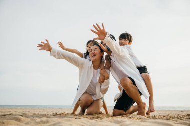 Kumsalda mutlu bir aile yaz tatilinin tadını çıkarıyor. Çocuklarla oynayan ve denize bakan ebeveynler. Seyahat ve rahatlama kavramı bu neşeli anda kaydedildi.