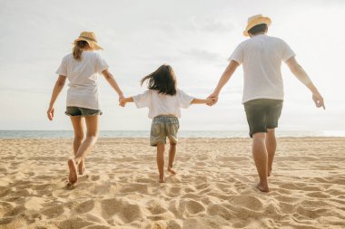 Mutlu Asyalı ebeveynler ve kızları sahilde eğleniyorlar. Anne ve babalarıyla birlikte kumsalda yürüyen bir çocuğun elini tutan küçük kızlar. Olumlu aile aktivitesi