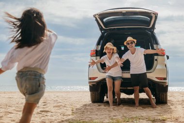 Üç kişilik Asyalı bir aile plajda arka arabada oynuyorlar ve genç bir kız arabaya doğru koşuyor. Baba ve anne, kızlarını karşılamak için kollarını açarlar. Yaz gezisi konsepti.