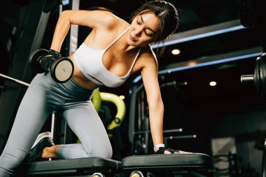 Spor salonundaki halterleri kaldıran Asyalı bir kadın, spor salonundaki dambıllarla güç antrenmanı yapan mutlu genç bir kadın, sağlıklı bir yaşam tarzı konsepti için ağırlık çalışması