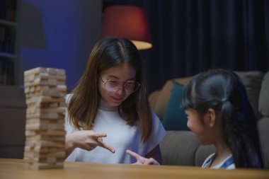 Asyalı genç anne, küçük kızıyla birlikte tahta blokta oyun oynuyor geceleri evde oturma odasında gülümseyen kadın, çocuklara tahta bloklar ve eğitim yapımında yardımcı oluyor.