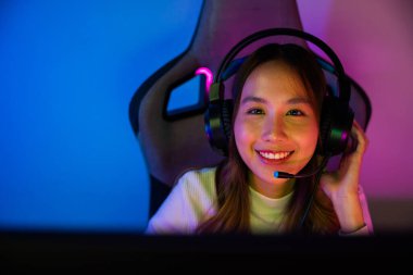 Asyalı mutlu oyuncu oyunu bilgisayar neon ışığı ile çevrimiçi video oyunları turnuvası düzenliyor, oyun kulaklığı takan gülümseyen genç kadın evde canlı yayın oyunları oynamak niyetinde, yazı tipi görünümlü