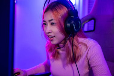 Young player woman wearing gaming headphones intend to do playing live stream games online at home, Happy Gamer endeavor plays online video games tournament with computer desktop with neon lights