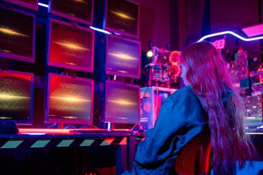 Bilgisayarında CCTV odası olan Asyalı bir kadın monitörde güvenliği sağlıyor, Hacker siyah ceket giyiyor ve uzun kızıl saçlı ve birden fazla bilgisayar monitörü var.