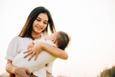 Gün batımından önce uyuyan oğlunu parkta tutan mutlu ve güzel bir annenin portresi. Anneler Günü 'nde anne gülümser ve bahçede yeni doğmuş bir bebekle dışarıda huzurlu bir şekilde eğlenir.