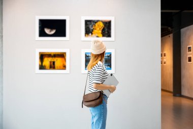 Asyalı bir kadın sanat galerisinde tablet tutuyor. Çerçeveli resimlerin önünde beyaz duvarda, fotoğraf çerçevesinde genç bir kadın sergi sanat galerisinde dijital kitap tutuyor.