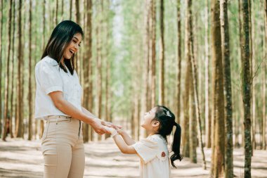 Asyalı anne ve kız bir ormanda el ele yürüyorlar, mutlu anne ve küçük çocuk el ele tutuşuyorlar, Aile Günü