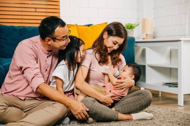 Evlerinin rahatlığında bir anne yeni doğmuş bebeğini bir şişeyle beslerken küçük oğlu ve kızı da aile fotoğraflarına mutluluk ve beraberlik katıyor..