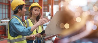 Endüstriyel mühendis ve işçi kadın işçisi metal levha ütü makinesi üzerinde çalışıyor, iki mühendis güvenlik kaskı takıyor fabrika imalatındaki makinelerden bahsediyorlar.