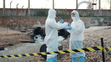 Nehirden gelen suyu test tüpü, koruyucu giysi içindeki bilim adamı veya biyolog ile örnekleyen ve maskesini koruyan ekolojist, analiz için endüstriden atık su örneği topluyor, sorun ortamı