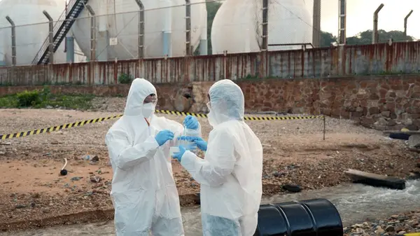 Nehirden gelen suyu test tüpü, koruyucu giysi içindeki bilim adamı veya biyolog ile örnekleyen ve maskesini koruyan ekolojist, analiz için endüstriden atık su örneği topluyor, sorun ortamı