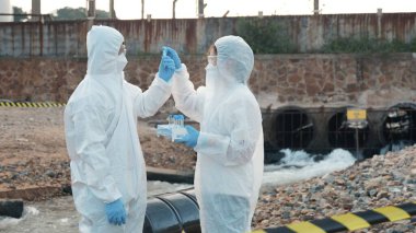 Nehirden gelen suyu test tüpü, koruyucu giysi içindeki bilim adamı veya biyolog ile örnekleyen ve maskesini koruyan ekolojist, analiz için endüstriden atık su örneği topluyor, sorun ortamı