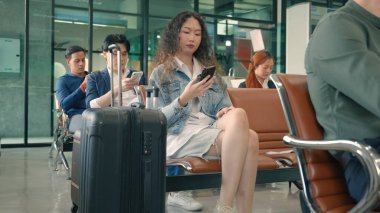Havaalanı kapısındaki yolcu kadın uçuş için akıllı telefon çalar. Hipster kadın terminal koridorunda oturur ve cep telefonu kullanır.