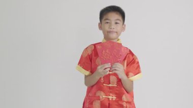 Yeni yılın kutlu olsun. Geleneksel kırmızı Cheongsam Qipao elbisesi içinde Asyalı bir erkek çocuğu, bereket ve zenginliği simgeleyen kırmızı bir paket para hediyesi taşıyor. Beyaz bir arkaplan üzerinde portre.