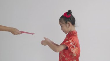 Çin Yeni Yılı. Mutlu Asyalı küçük kız kırmızı Cheongsam Qipao giyer. Kırmızı Hongbao zarf paketini beyaz arka plandaki şanslı para için annesinden verir.