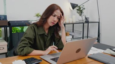 Mutsuz, güzel, meşgul bir kadın masa başında oturmuş internetten araştırma yapıyor Asyalı genç iş kadını bilgisayarla çalışıyor ev işlerinde çalıştığını düşünüyor.