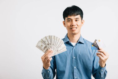 Dolarları ve kredi kartını güvenini göstermek için kullanmayı seçen mutlu bir gencin portresi. Stüdyo çekimi beyaz, finansal karar verme mekanizmasını vurguluyor.