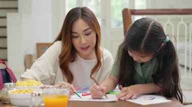 Evde renkli kalemlerle çizim yapan iki Asyalı anne ve kız çocuk resim öğreten aile kızı mutfakta renkli kalemler kullanıyor.