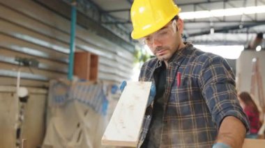 Sarı kasketli ve güvenlik gözlüklü marangoz atölyede iki tahta parçasına klemp takmış. İşçi Bayramı temaları için mükemmel, marangozluk uzmanlığı ve zanaatkarlığı vurgulanıyor