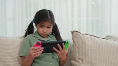 Kanepede otururken tablet kullanan mutlu Asyalı genç kız evdeki oturma odasında video oyunu oynayan çocuk, online oyun konsepti.