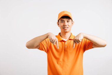 Asyalı gülümseyen genç teslimatçı boş ellerle bir şeyi işaret ediyor stüdyo izole edilmiş beyaz arka plan, mutlu yaşam tarzı erkekler turuncu gömlekli birini taşıyor işaret parmağı.