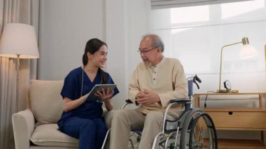 Hasta dosyasıyla dijital tableti elinde tutan Asyalı kadın doktor tekerlekli sandalyede oturan yaşlı adama tedavi sonuçlarını açıklıyor.