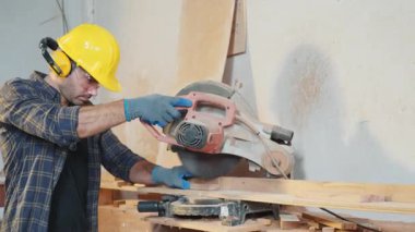 Odun kesmek için testere kullanan sarı şapkalı bir adam. İnşaat, ev tadilatı ve ahşap işçiliği için ideal elektrikli aletlerle kusursuz kesim teknikleri, Ulusal Marangozlar Günü