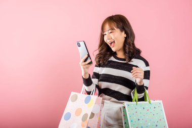 Asyalı mutlu genç bayan alışverişçi gülümsüyor çevrimiçi alışveriş çantalarını tutarken heyecanlanıyor çok renkli ve akıllı telefon elinde, pembe arka planda izole edilmiş, cep telefonundan memnun.
