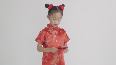 Kırmızı Cheongsam 'lı gülümseyen Asyalı kız elinde angpao kırmızısı paketi tutuyor. Parasal hediyeleri sembolize ediyor. Beyaz bir arka planda izole edilmiş geleneksel elbiseli bir çocuğun portresi..