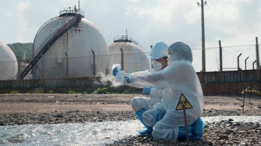 Ecologist sampling water of toxic chemicals from river touching screen on digital tablet, Biologist wear protective suit and mask collects sample of waste water from industrial, problem environment
