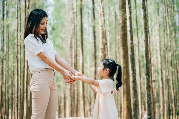 Asyalı anne ve kız bir ormanda el ele yürüyorlar, mutlu anne ve küçük çocuk el ele tutuşuyorlar, Aile Günü