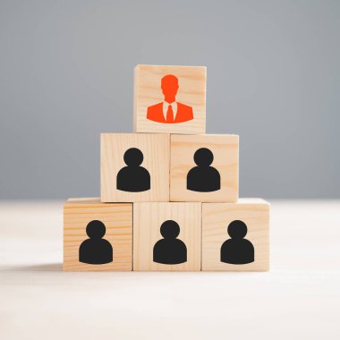 İşletme ortamında farklı düşünce ve insan gelişimi kavramını temsil eden, ahşap bir bloğa basılmış bir grup personel çalışan simgesinden bir kırmızı yönetici simgesi öne çıkıyor.