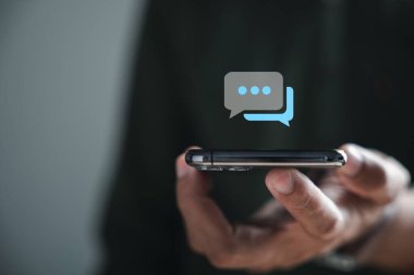 Akıllı telefonuyla canlı sohbete katılan bir adam sosyal iletişim ve sohbet kavramlarının birleşmesini sembolize eder. Sohbet kutusu simgeleri ortaya çıkıyor, teknolojinin sosyal arabuluculuğa kusursuz entegrasyonu.