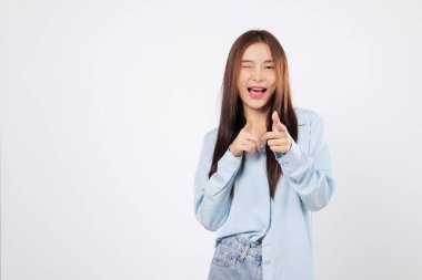 Dost canlısı bir kadın göz kırparken ve gülümserken yüzsüz bir jest yapar, sanki beyaz arka planda tek başına ne yapıyorsun ya da ne yapıyorsun der gibi şakacı bir şekilde işaret eder.