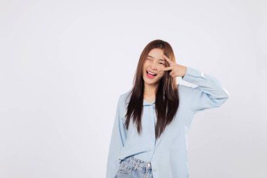 Zafer jesti, gülümseyerek, huzur ve neşe içinde. Beyaz arka planda izole edilmiş zafer atmosferi, iyimser Asyalı kadın pozitif titreşimler ve heyecan ifade ediyor.