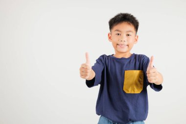 Beyaz arka planda izole edilmiş bir stüdyo portresindeki kendine güvenen Asyalı genç çocuk onay işareti yapıyor, anlaşma ve başarıyı simgeliyor. birincil çocuk gülümsemesi pozitiflik ve memnuniyet yayar