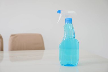 Mutfak masasında beyaz tetik olan mavi cam sprey şişesi beyaz arka planda. Şişe temiz mavi sıvıyla dolu, temizlik konsepti.