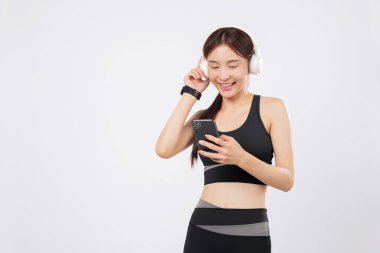 Telefonda başvuru müziğine göz gezdirirken spor giyim bölümündeki bu Asyalı kadın antrenman sırasında kulaklıklarıyla neşeyle dinliyor. izole stüdyo beyaz arkaplan