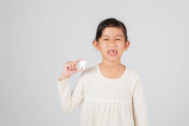 Çocuk dişleri dökülmüş şekilde gülümsüyor, dişçi konuşması için elinde bir model tutuyor. Diş bakımını, çocuk gelişimini ve doğal diş kaybını açıklamak için diş boşluğunu gösteriyor. izole edilmiş beyaz arkaplan