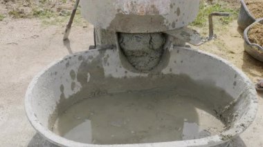 Gri harcı bronz kumla harmanlayan bir çimento karıştırıcısı. Bıçakları tek bir beton karışımı sağlıyor..
